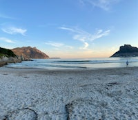 a person is flying a kite on a beach with mountains in the background
