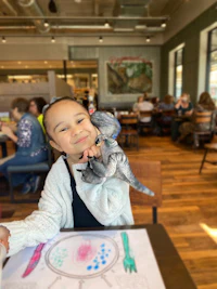 a little girl sitting at a table holding a stuffed animal