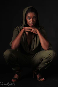 a black woman in a green hoodie crouching on a black background
