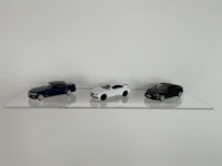 three toy cars on a clear shelf in front of a white wall