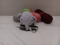 a crocheted elephant with scissors and yarn on a bed