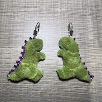a pair of green dinosaur earrings with purple sequins