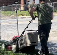 a man pushing a lawn mower in front of a fence