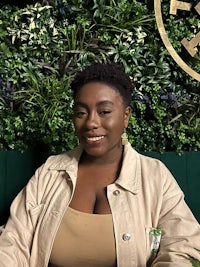 a woman in a tan jacket sitting in front of a green wall