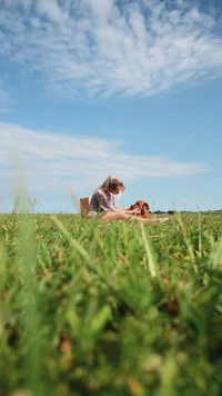 a girl is sitting in a grassy field with a dog