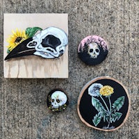 a skull, a sunflower, and a crow painted on a piece of wood