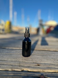 a black bottle sitting on a wooden deck with a boat in the background