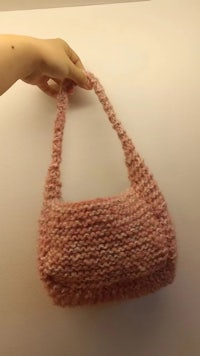 a hand holding up a pink knitted bag