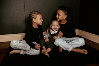 three boys sitting on the floor in front of a black background