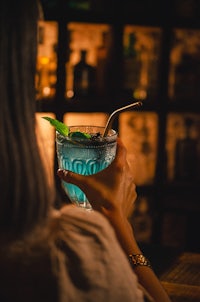 a woman is holding a cocktail in front of a bar