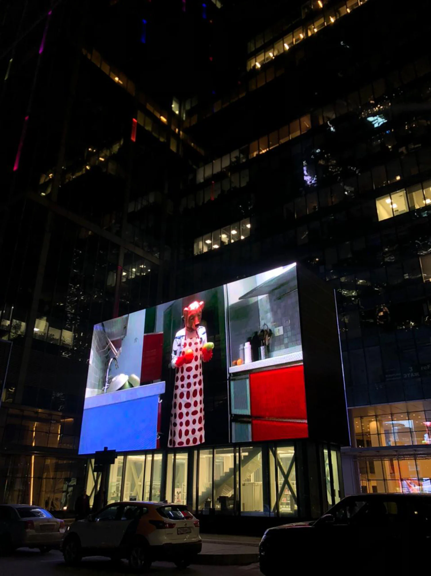 a woman in a red dress is on a large screen in front of a building