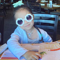a little girl wearing sunglasses at a table in a restaurant