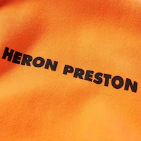 a close up of an orange sweatshirt with the word heron preston on it