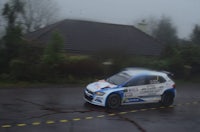 a blue and white rally car driving on a wet road
