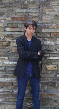 a young man leaning against a stone wall