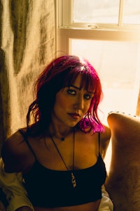 a woman with pink hair sitting in front of a window