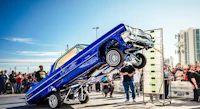 a blue car doing a flip in front of a crowd of people