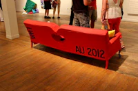 a red couch in an art gallery with people standing around it