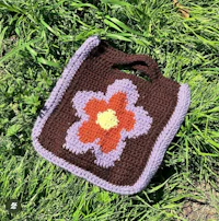a crocheted flower bag is laying in the grass