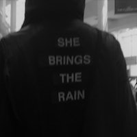 a black and white photo of a man wearing a jacket that says she brings the rain