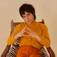 a man in an orange sweater sitting in a chair