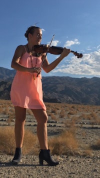 a girl in a pink dress playing a violin in the desert
