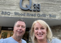 two people standing in front of the q39 bbq & wood fired grill