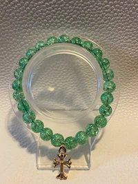 a green beaded bracelet with a gold cross charm