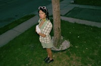 a woman in a green shirt standing next to a tree