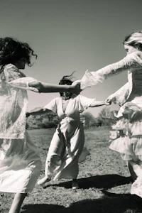 three women in white dresses dancing in a field