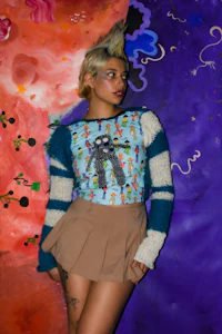 a woman wearing a sweater and skirt posing in front of a colorful wall