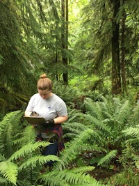 a woman is standing in a forest with ferns
