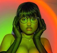 a woman with glasses and gloves posing in front of a neon light