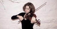 a woman playing a violin in front of a white wall