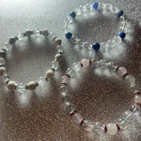 three bracelets with clear and blue beads on a silver surface