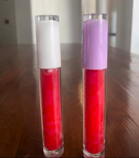 two bottles of lip gloss sitting on top of a wooden table