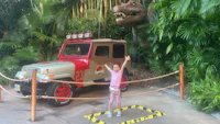 a little girl standing in front of a jeep in a park