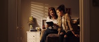 two women sitting in a room looking at a tablet
