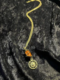 a gold necklace with an orange stone and a sun
