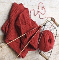 red yarn and knitting needles on a wooden table