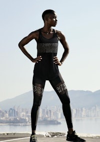 a woman in a black tank top and leggings posing in front of a city