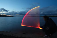 a man crouching down next to a body of water