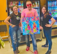 a group of people standing in front of a refrigerator holding a painting