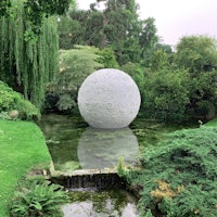 a white sphere sits in a pond in a garden