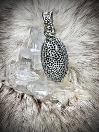 a silver pendant with a black and white pattern on it