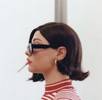 a woman wearing glasses and a striped shirt smoking a cigarette