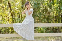 a woman in a white dress leaning on a fence