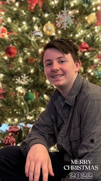 a young boy is posing in front of a christmas tree