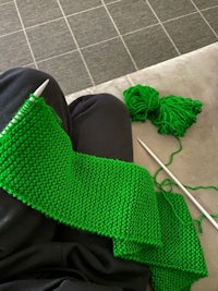 a person knitting a green scarf on a couch
