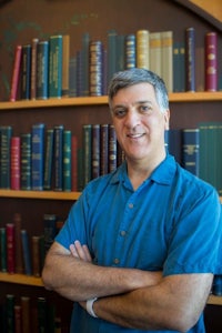 a man with his arms crossed in front of a book shelf